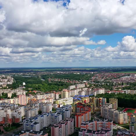 Urban background under beautiful sky. Modern city with high-rise buildings on green fields background. Aerial view. Camera rising up.