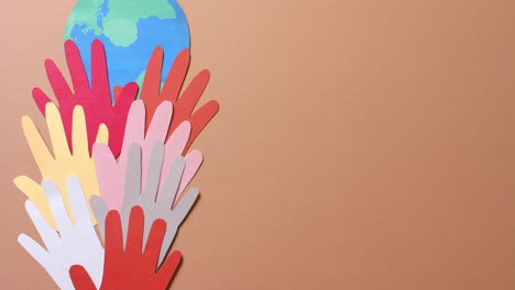 Close up of hands together with globe made of colourful paper on brown background with copy space