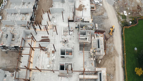 aerial reveal over new commercial building under development with employed union construction site workers operating heavy machinery industrial jobs urban real estate apartment housing flyover 4k