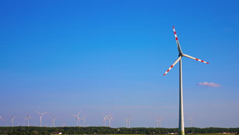 tall wind turbine rotating in the blue clear sky. wind farm in the fields at backdrop. low angle view.