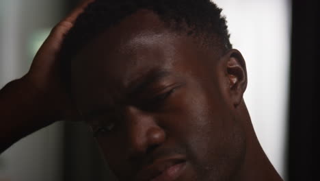 close up of unhappy and depressed young man sitting on sofa at home at night closing eyes and putting head in hands