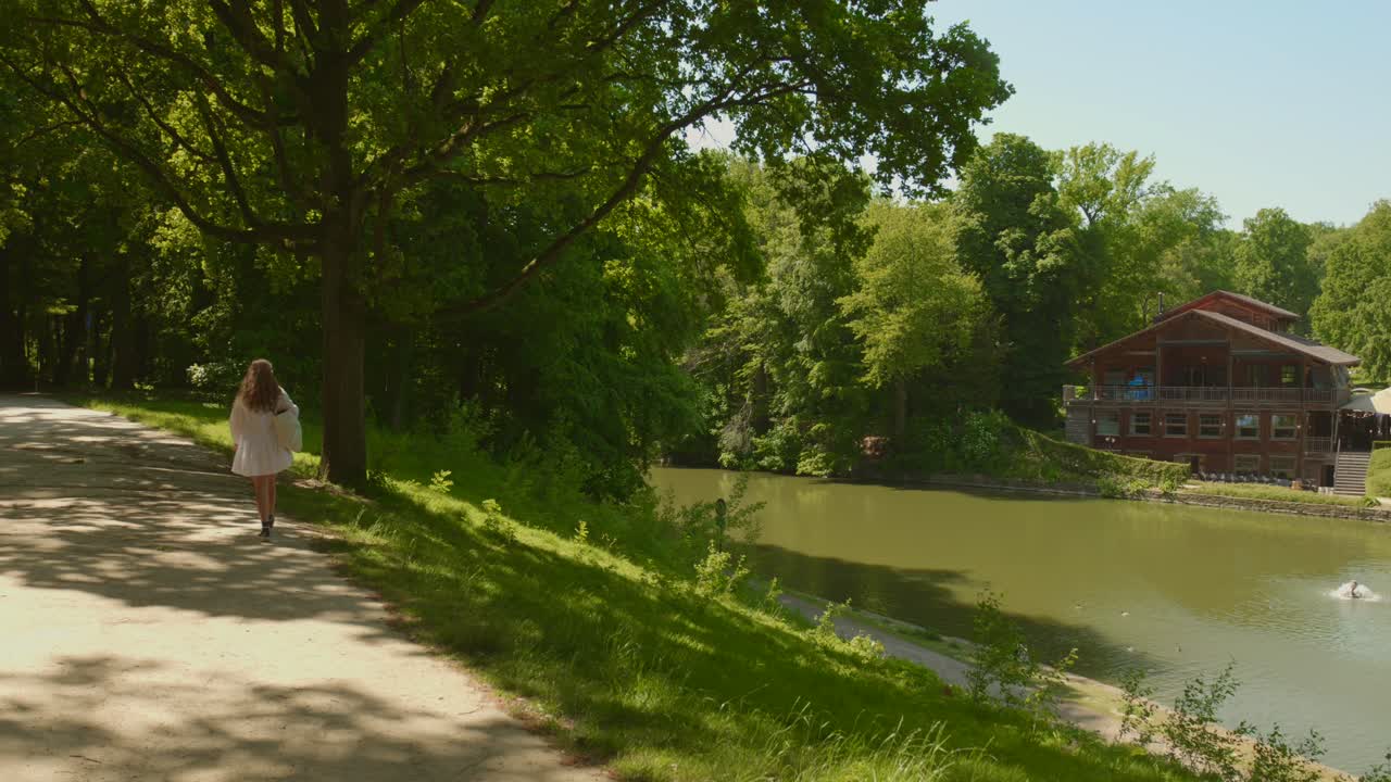 Beautiful woman in a white dress walking next to the Robinson restaurane chalet in Bois de la Cambre in Brussels, Belgium