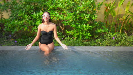 Asian-smiling-girl-sitting-on-pool-edge-plays-with-water