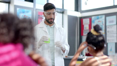 in a school classroom, a young biracial teacher demonstrates a chemistry experiment