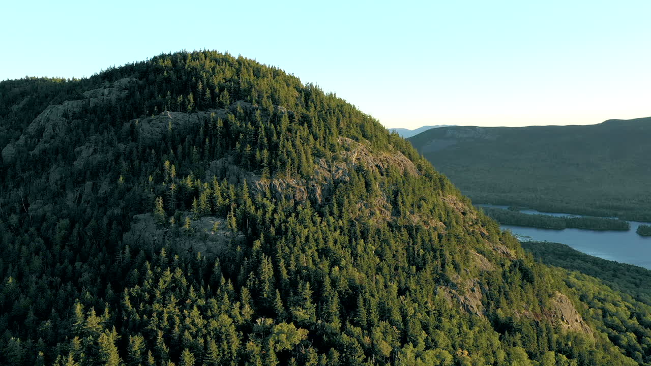 toma aérea de un dron orbitando alrededor del pico de la montaña bore cubierta de espesos árboles verdes sobre el bosque y los lagos en el desierto de maine.
