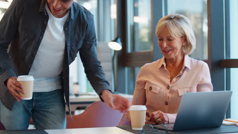 mature businesswoman mentoring younger male colleague working on laptop at desk