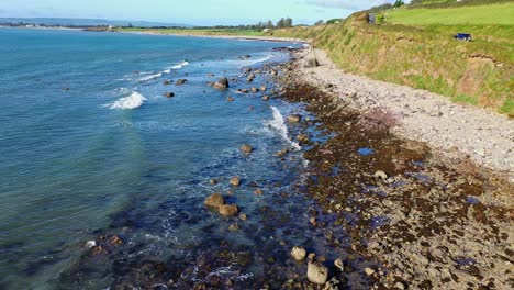 aerial view of waves, rocky shoreline and costal road with car moving along the south coast of ireland