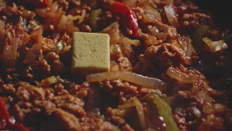 Adding-stock-cube-to-a-recipe-of-meat-and-vegetables-being-cooked,-macro-shot