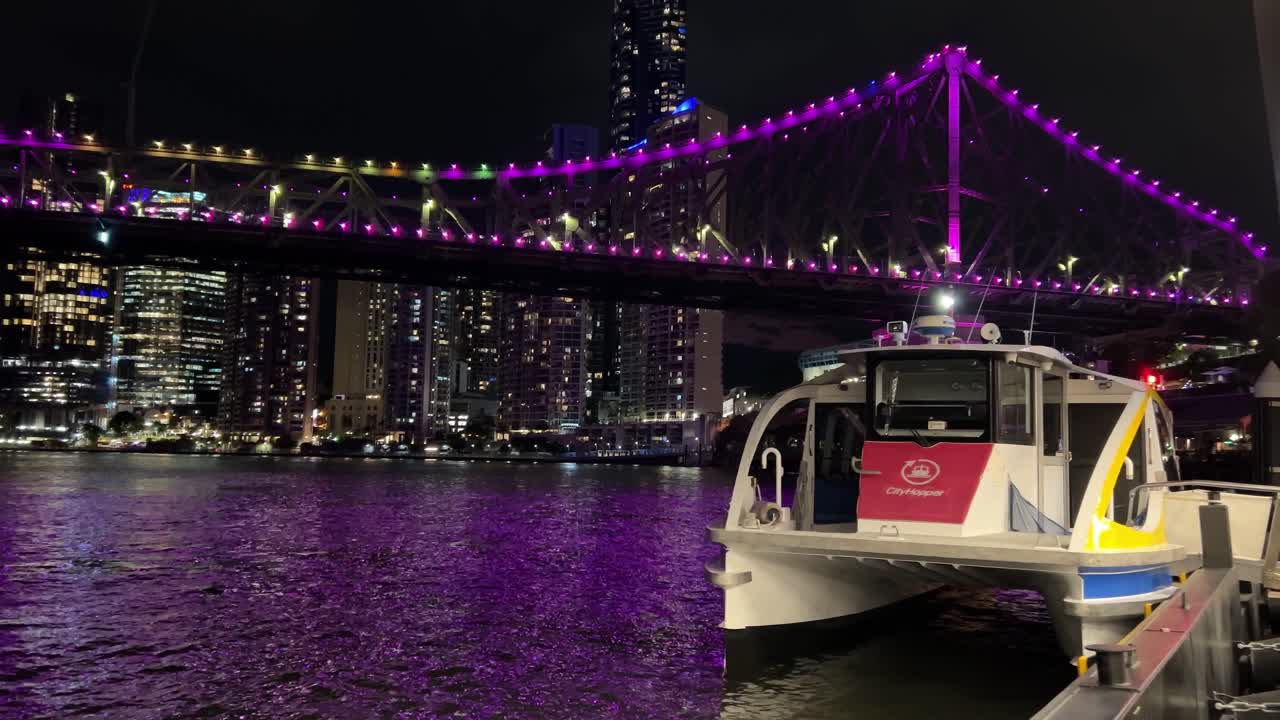 cityhopper atracó en la terminal de ferry de howard smith wharves esperando su viaje programado por la noche con el icónico puente de la historia iluminado en púrpura, reflejado en el agua ondulada del río y el paisaje urbano del centro urbano