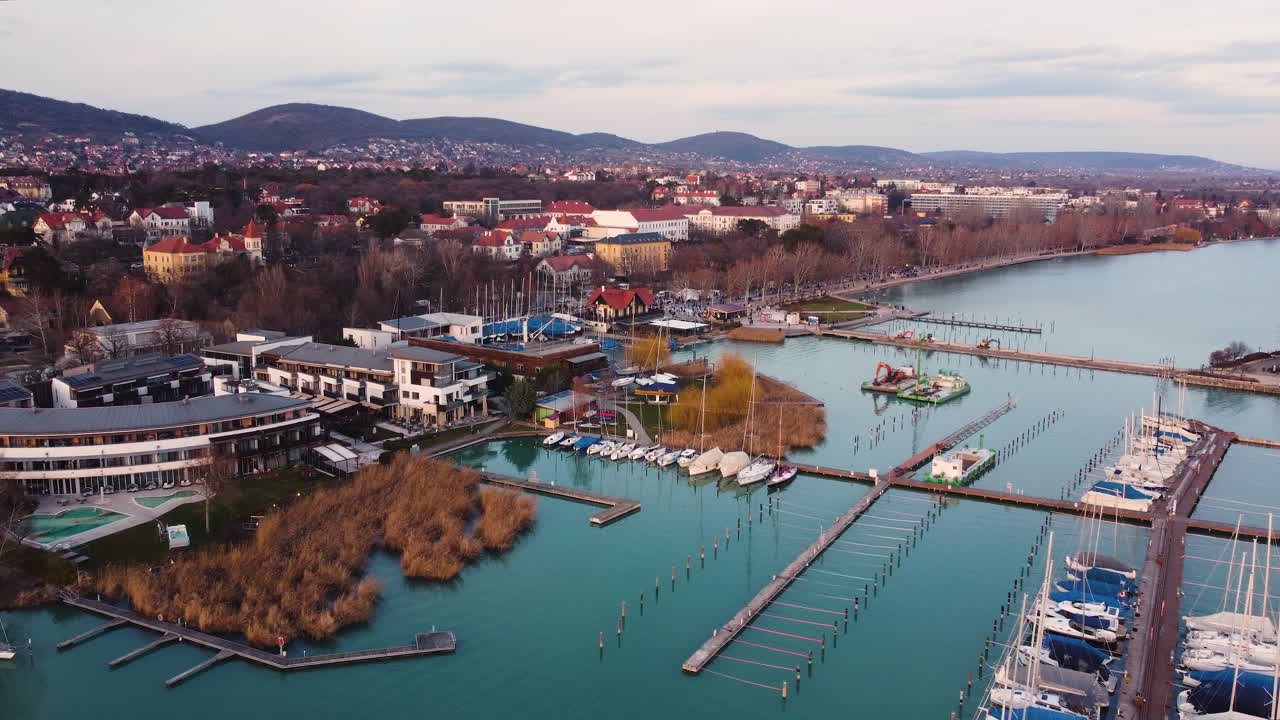 Drone shot over marina in Balatonfured with warm tones, colorful buildings, and boats