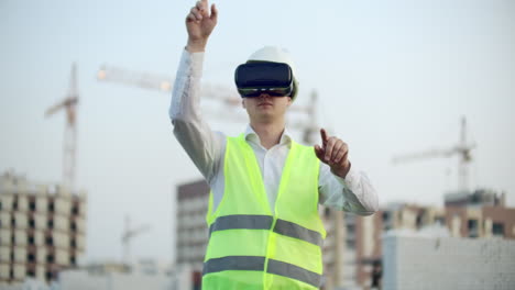 Retrato-De-Un-Inspector-Masculino-Analizando-El-Trabajo-De-Los-Constructores-Utilizando-Gafas-De-Realidad-Virtual.-Un-Hombre-Con-Casco-Y-Chaleco-Protector-Se-Para-Con-Gafas-Vr-Y-Mueve-Las-Manos.