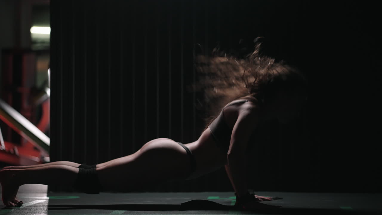 A sexy athletic woman in lingerie dances wet in oil in the gym near the gym near the gym benches and barbells.