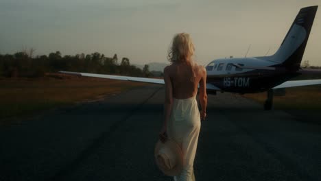 woman walking on an airport runway towards a small plane at sunset