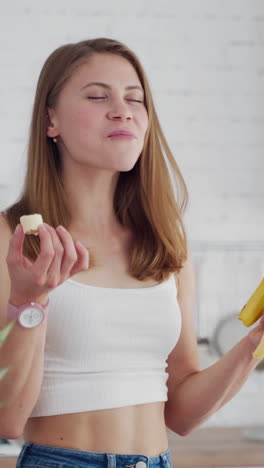 pretty woman enjoys eating banana. young female in casual clothing eats fresh fruit in the kitchen. healthy food concept. vertical video