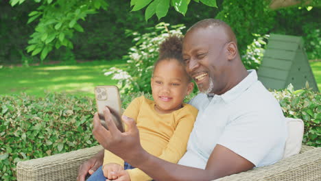 grandfather with granddaughter taking selfie on mobile phone in garden at home