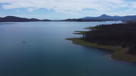 Flying-over-lake-Plastira's-shoreline-and-people-riding-water-bikes