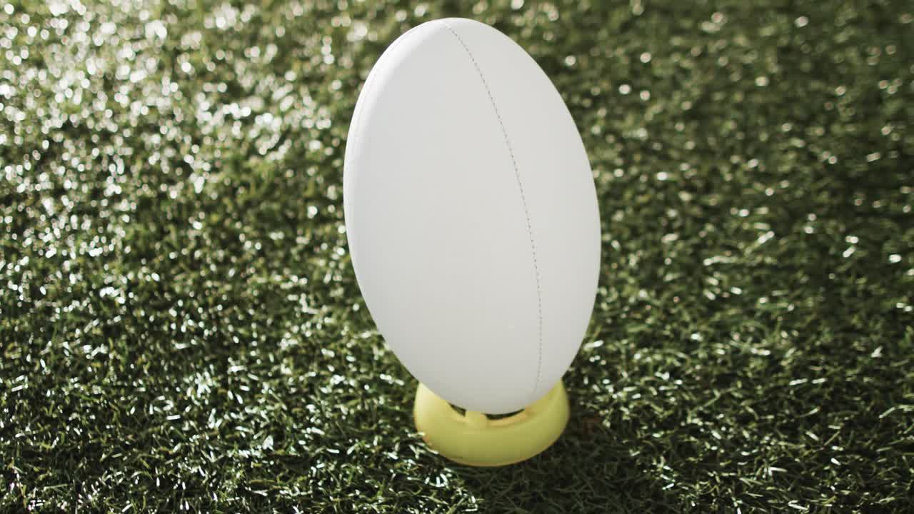 pelota de rugby blanca en patear tee en la hierba iluminada por el sol con espacio de copia, cámara lenta