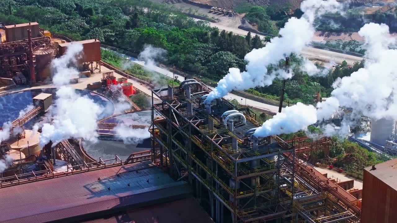 Metallic vents release white steam at the Barrick Gold mining complex for gold and silver extraction in Cotuí, Dominican Republic. Surrounded by tanks, pools, and vegetation.