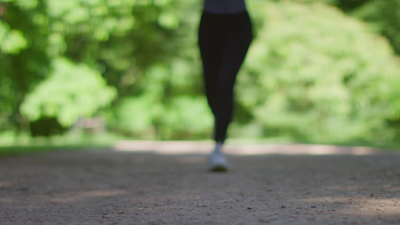 Ground Level Shot Of Young Woman Exercising Running Towards Camera Into Focus In City Park 2