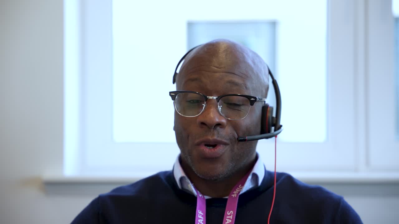 Selvsikker, smilende svart mann med headset og snor, som deltar i et virtuelt møte i et kontormiljø
