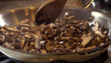 cook spreads fried mushroom slices around frying pan with wooden spoon