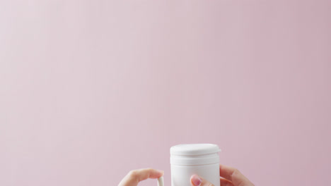 Video-of-hands-holding-white-pill-box-and-white-pill-on-pink-background-with-copy-space