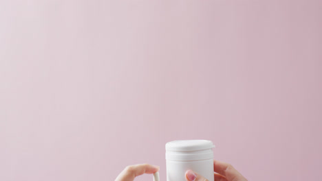 video de manos sosteniendo una caja de pastillas blancas y una pastilla blanca sobre un fondo rosa con espacio para copiar.