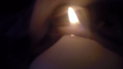 smoke surrounding a burning white candle close up in a dark room