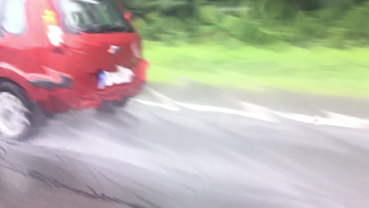 Cars driving fast in a right lane in a rainstorm viewed as distorted through drips of water on a passenger window