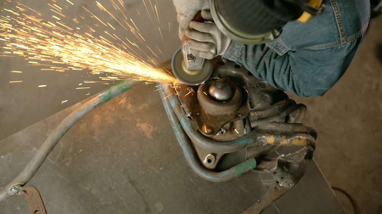 cerrajero lija el metal decorativo inacabado escultura de pez steampunk por molinillo eléctrico con muchas chispas en cámara lenta, metalurgia en taller, 4k 60p prores hq