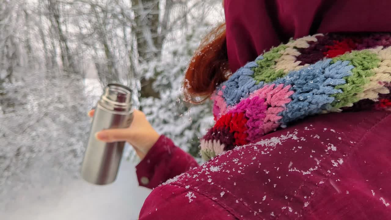 Woman drinking hot drink from thermos outside while snowing on winter day, close up