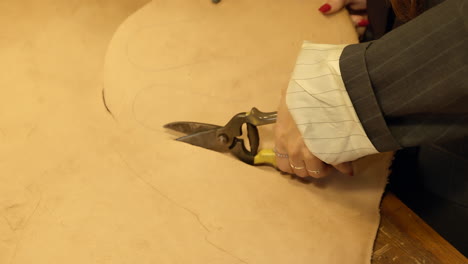 female hands close up cutting leather pattern with shears making shoes in workshop