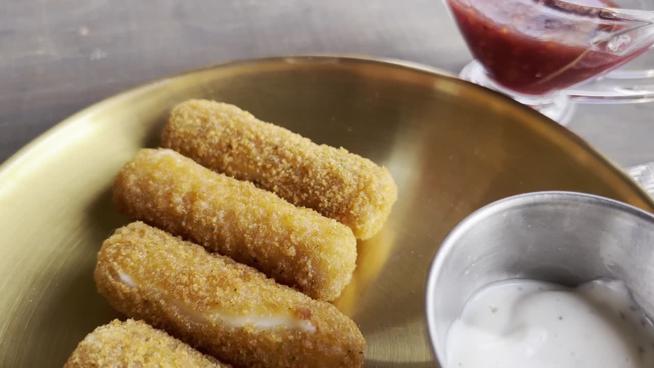 Crispy mozzarella sticks served with ranch and marinara on golden plate indoors