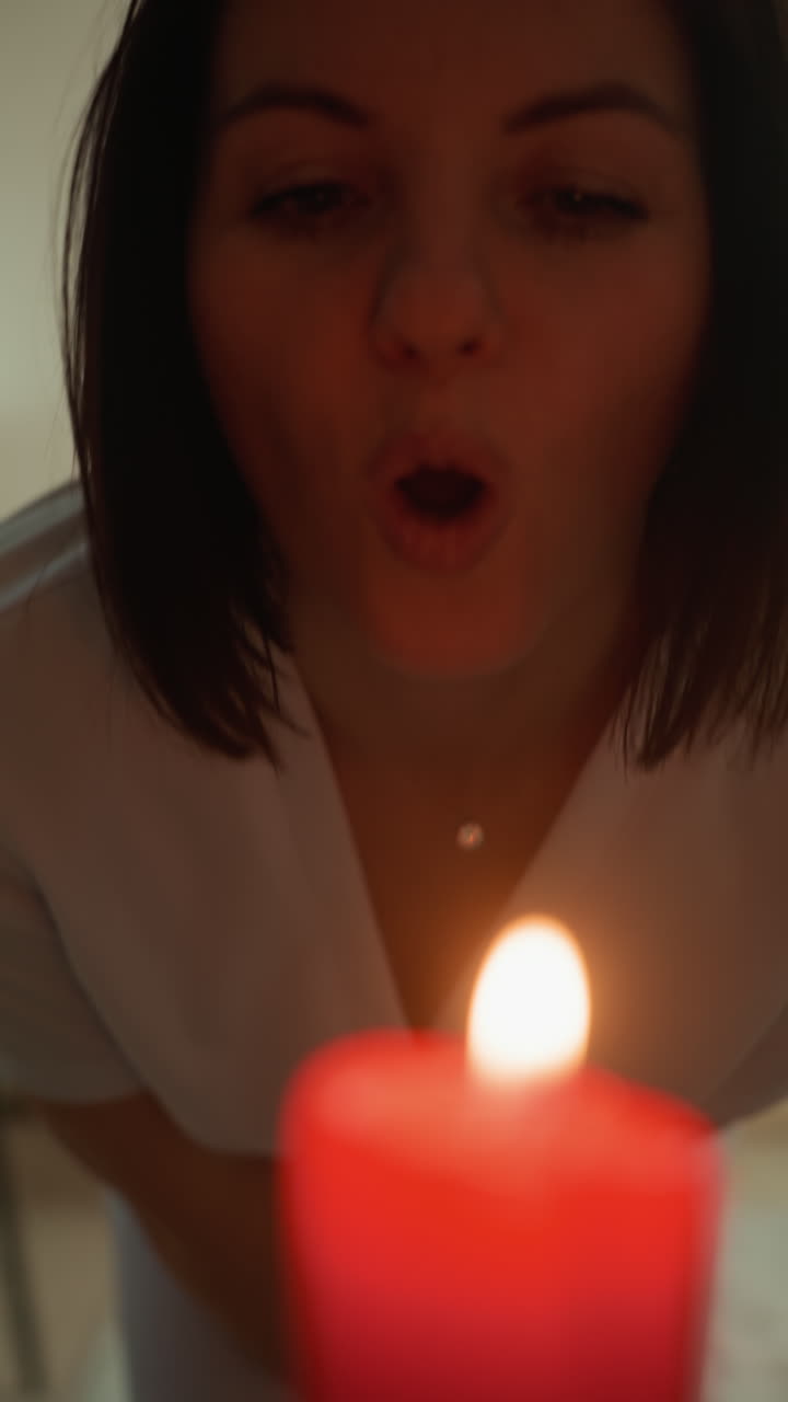 terapeuta caucasiana com vela acesa soprando a chama para criar fumaça calmante, sorriso gentil perto da câmera, sala de spa com maca de tratamento e toalha, brilho quente e iluminação suave, microcorrente