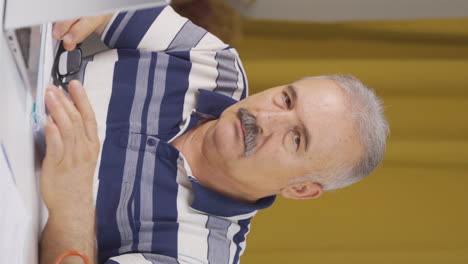 video vertical de un anciano trabajador de oficina en casa mirando aburrido a la cámara.