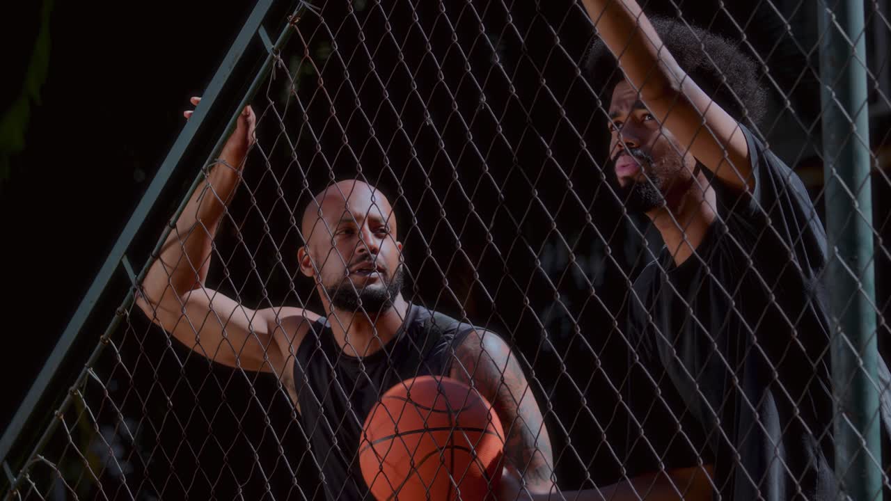 Two Men with a Basketball Looking Through a Chain-Link Fence