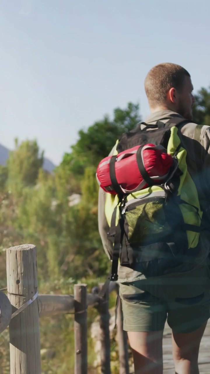 Video verticale: Escursionista che cammina su una passerella, telecamera bassa sullo zaino con panoramica all'indietro, bagliori davanti all'escursionista, viaggio.