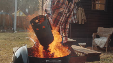 man pouring charcoal from chimney starter into grill