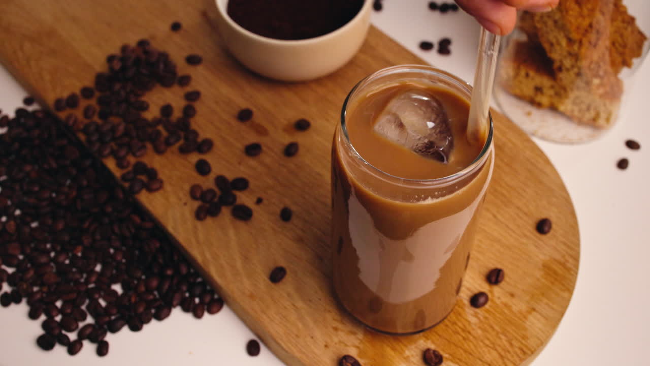 Caffè freddo mescolato a mano con una cannuccia su una tavola di legno