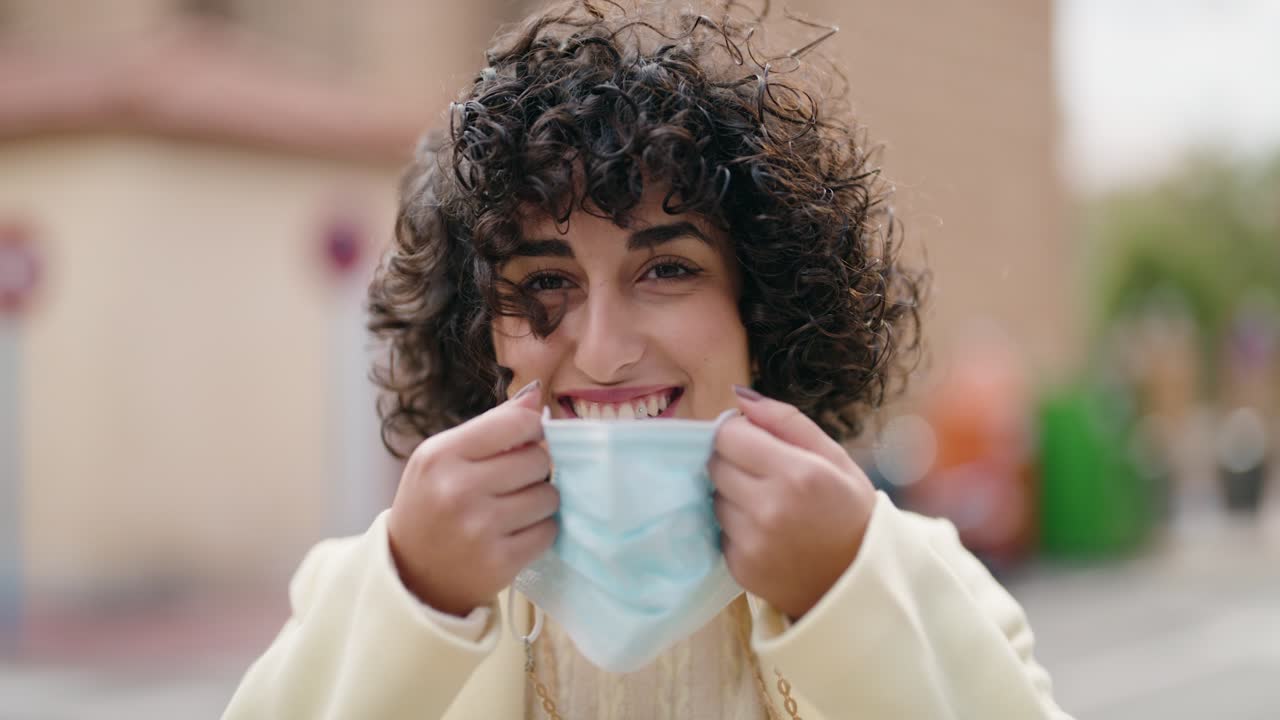 mujer joven sonriendo confiada usando máscara médica en la calle