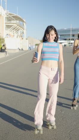 three young women roller skating and using phones outdoors