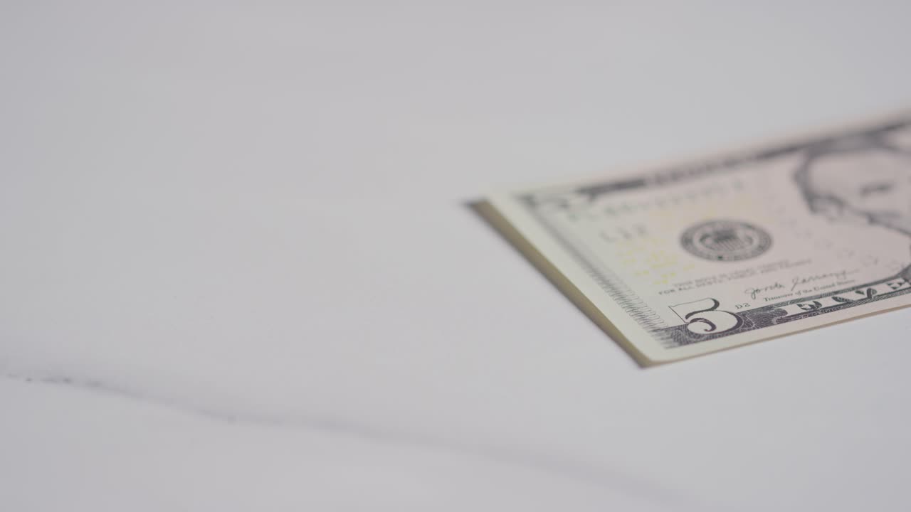 primer plano de moneda de la mano agarrando un billete de 5 dólares sobre fondo de mármol