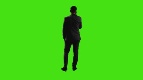 rear view of businessman talking on mobile phone standing against green screen with low key lighting