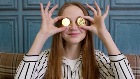 woman freelancer holding two gold coins at home, successful developer programmer, earning bitcoins