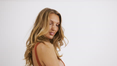 chica rubia caucásica con el pelo largo posando en un traje de una pieza de bikini naranja, con un fondo blanco infinito