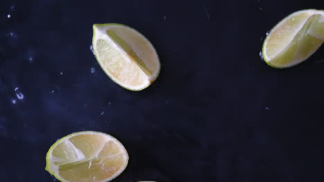 Fresh-slices-of-green-lime-fruit-dropping-into-water-with-splashes-in-slowmotion