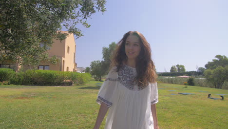 a young woman walks and smiles in a beautiful garden setting with green grass and trees.