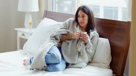 Thoughtful-woman-wrapped-in-blanket-having-coffee-4k
