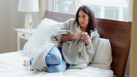 mujer pensativa envuelta en una manta tomando café 4k