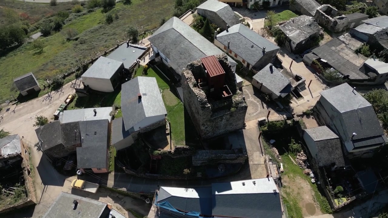 Top-down drone view of Torre do Castro surrounded by village houses and rooftops, revealing the medieval stone tower within the compact settlement above O Barco de Valdeorras